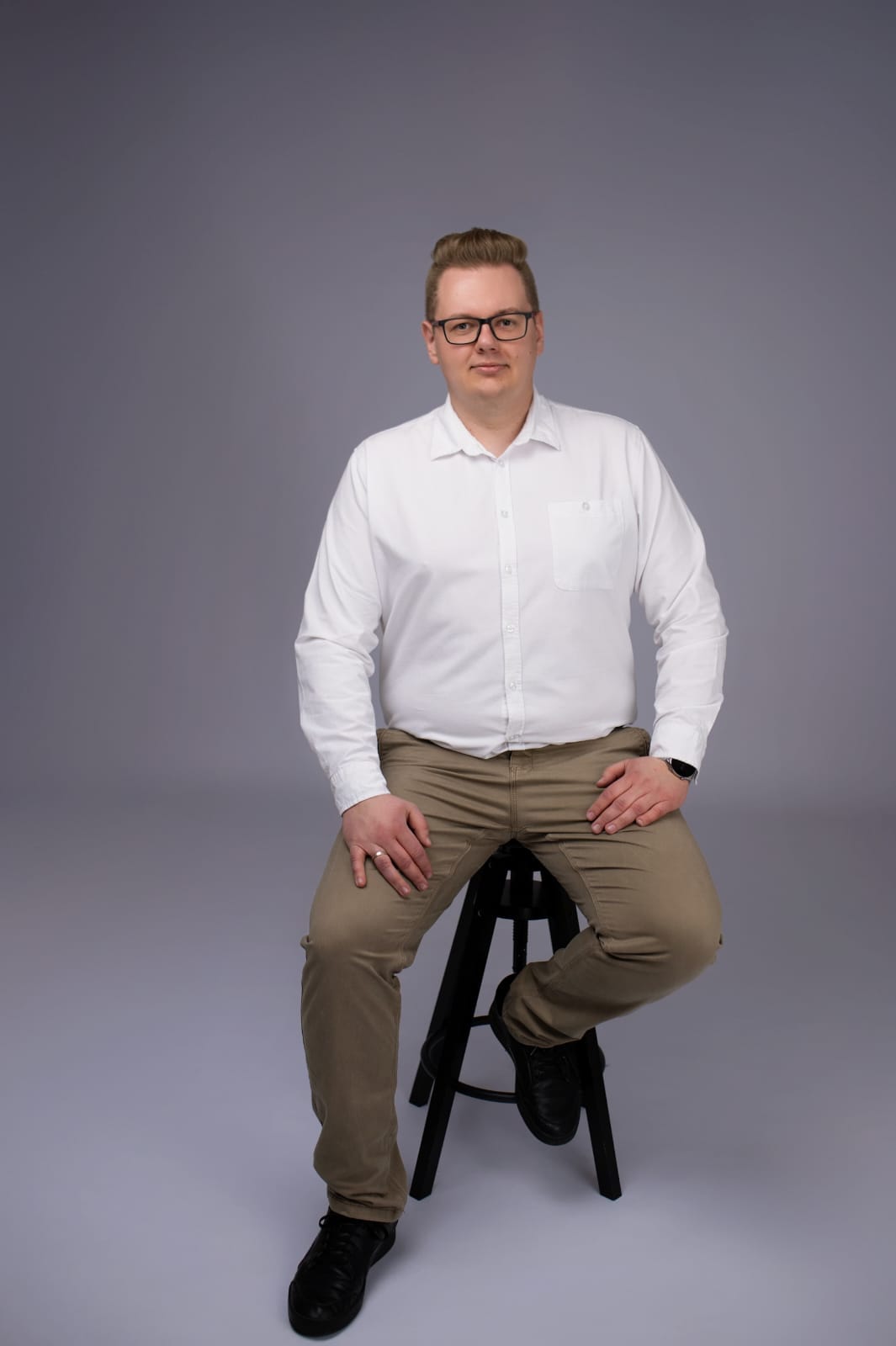 mężczyzna w białej koszuli, siedzi na krześle i pozuje