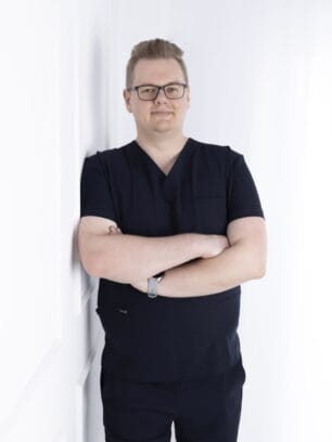 mężczyzna w uniformie medycznym, stoi oparty o ścianę uśmiecha się